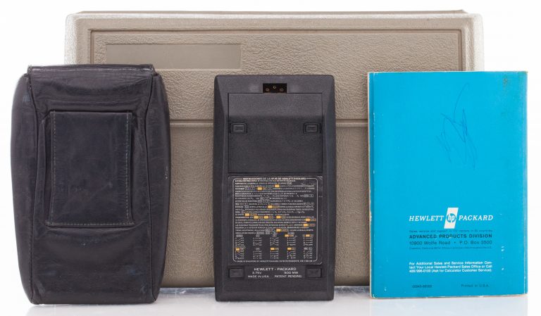 The back of the HP 45 calculator, with carrying pouch and owner's handbook in front of a plastic storage case.