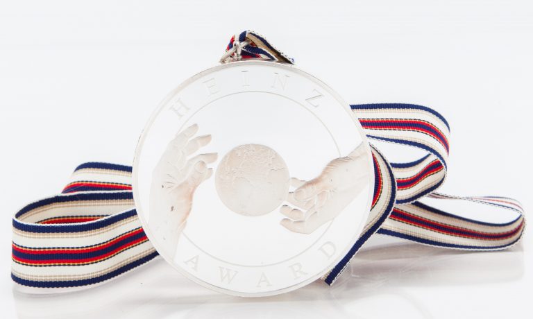 Front of the Heinz Chairman's Medal depicting the Earth and two hands along with the words Heinz Award on top/bottom.