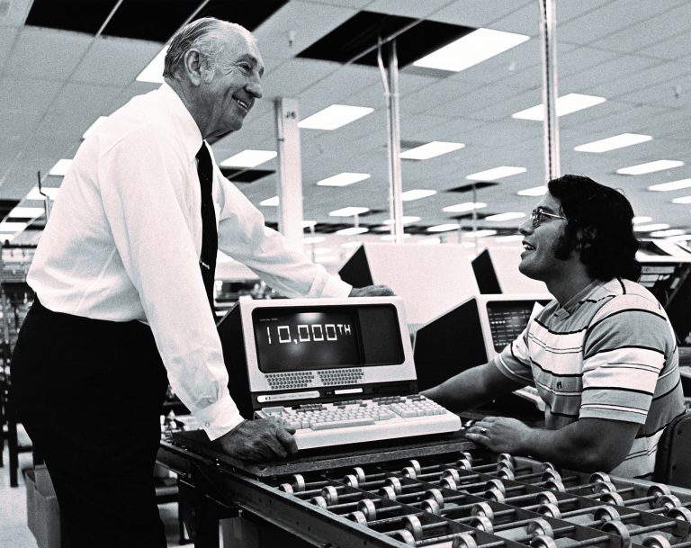 Dave Packard speaking with an employee near a CRT monitor displaying 10,000th on its screen in 1977.
