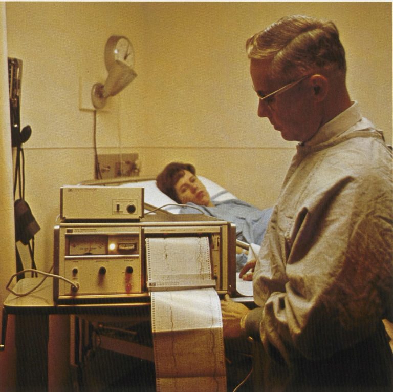 A doctor checking the printed readout from the HP 8020A cardiotocograph with a woman in bed in background.