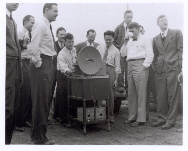 Photo of a microwave signal generator with a crowd gathered around during a demonstration in 1947.