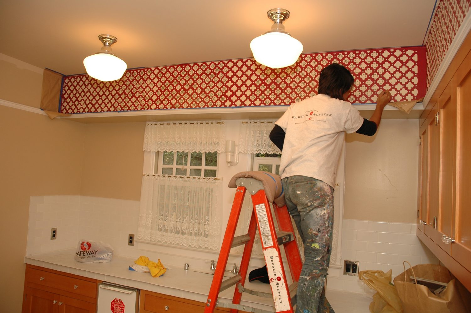 Photo of a worker painting a pattern in the Addison Avenue kitchen to replicate the wallpaper from the Packards' time there.