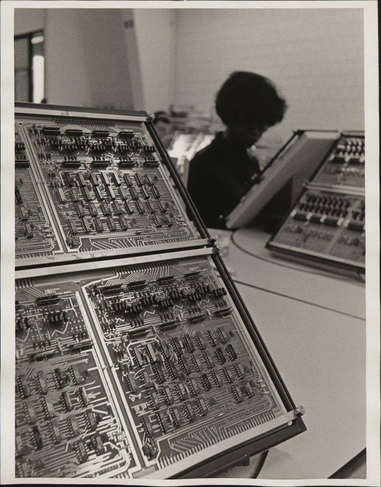 A photo of two computer circuit boards in the foreground and HP employee working in the background.