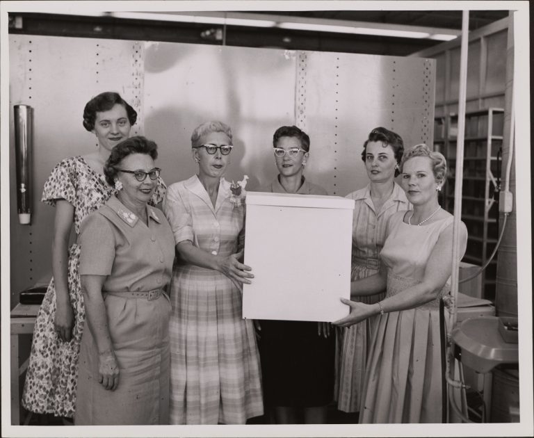 Photo of several women gathered at a celebration and two women holding a large white box.