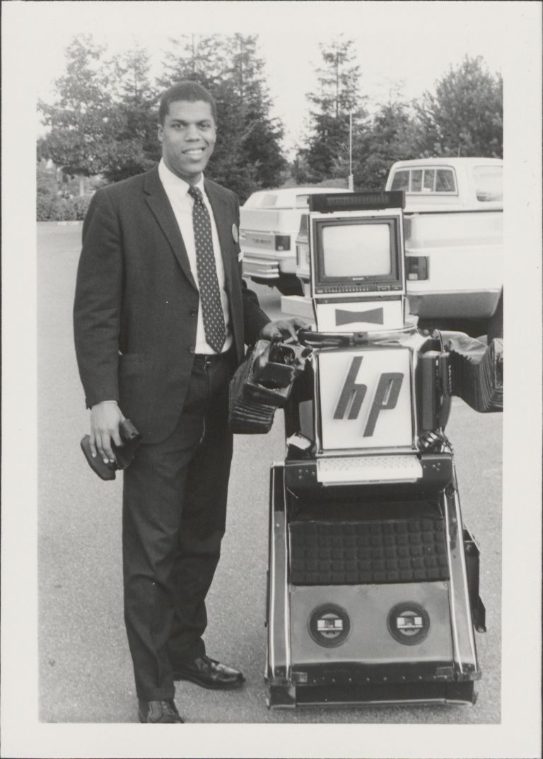 An HP employee poses next to a robot featuring the HP logo on its chest and a monitor for a head.