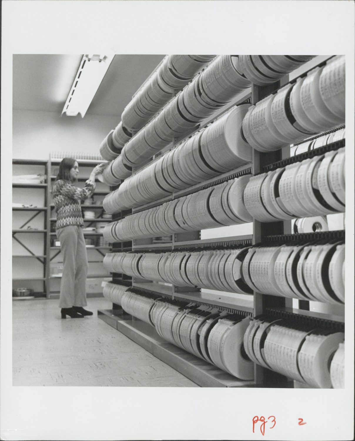A woman goes through rows of magnetic tape reels in a storage room.