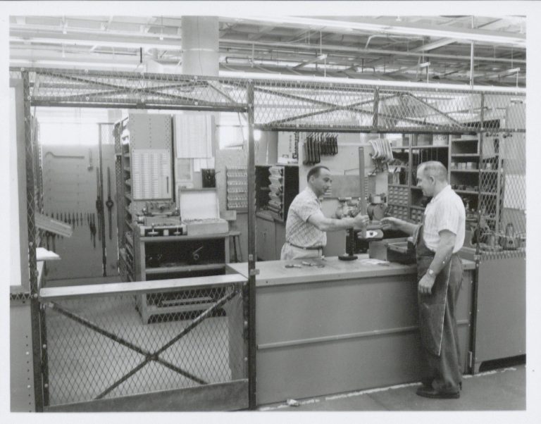 Photo of the Hewlett-Packard toolroom taken in 1961. A man behind the counter is handing a tool to an HP worker.