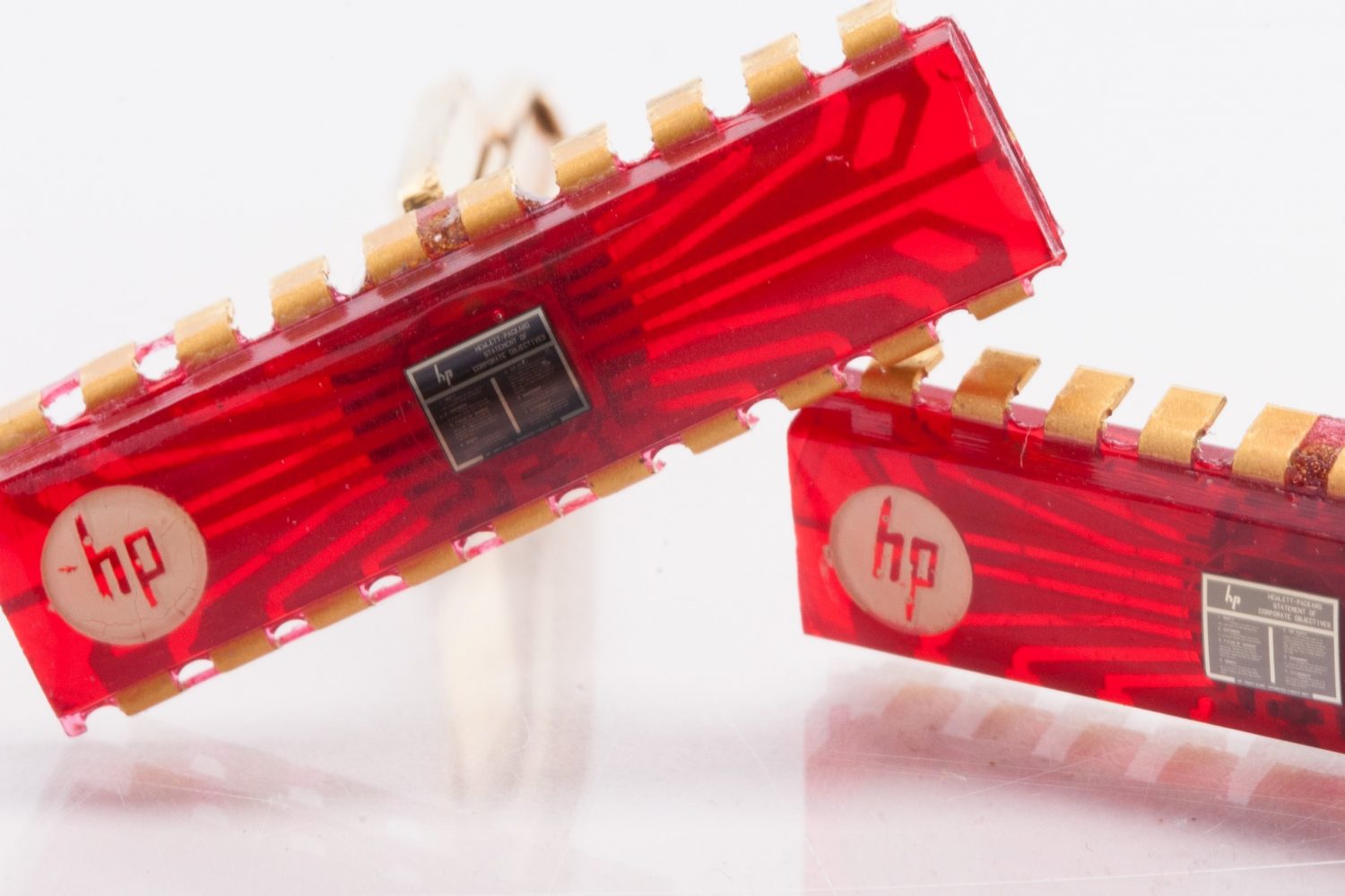 Two gold HP cufflinks with red chips and company objectives printed on a tiny chip in the center of each one.