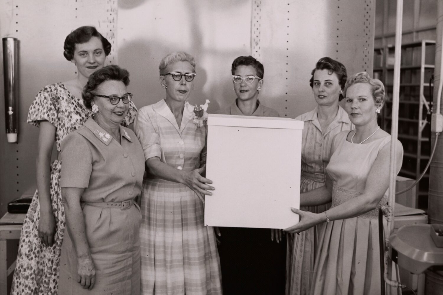 Photo of several women gathered at a celebration and two women holding a large white box.