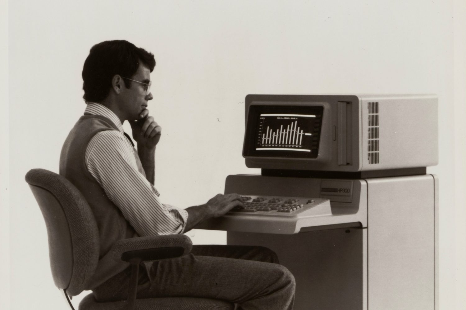 A man sitting at the HP 300 terminal with built-in desk and keyboard.