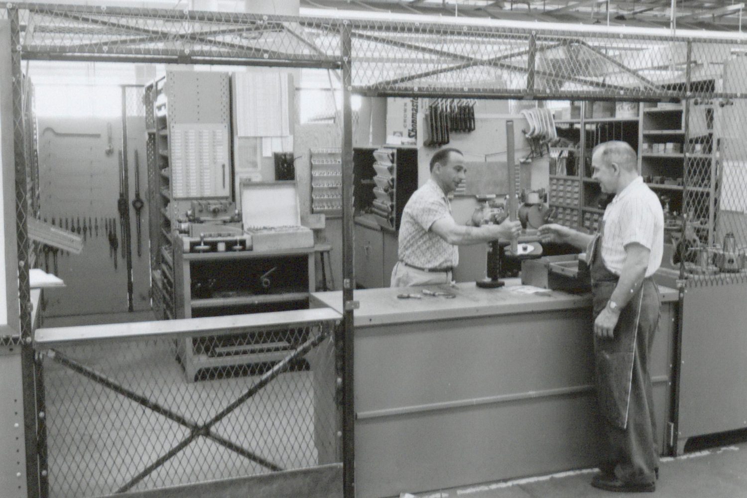Photo of the Hewlett-Packard toolroom taken in 1961. A man behind the counter is handing a tool to an HP worker.