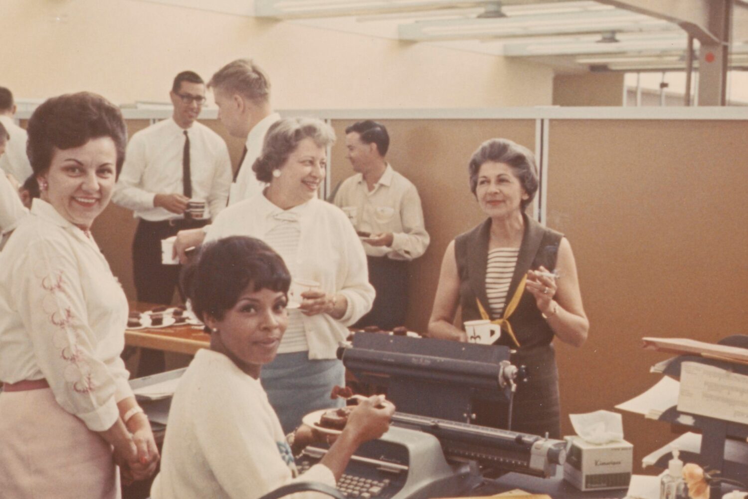 A group of HP employees have cake and coffee in a cubicle in 1964.