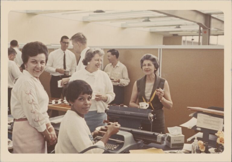 A group of HP employees have cake and coffee in a cubicle in 1964.