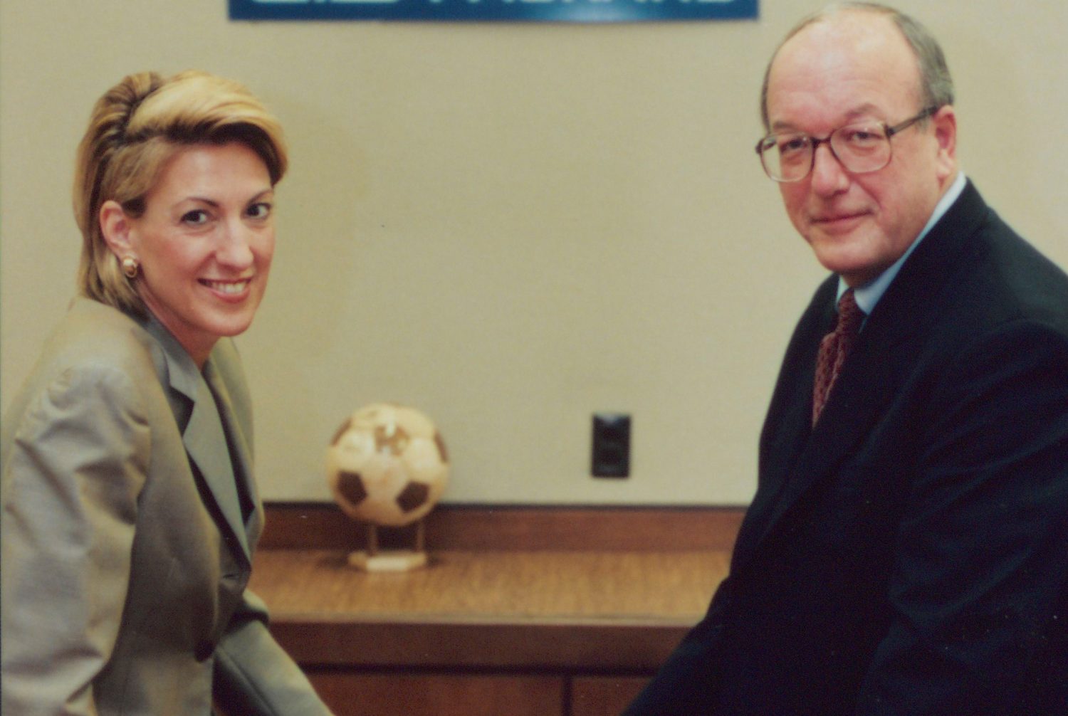 Carly Fiorina and Lew Platt seated on a table next to an HP laptop.