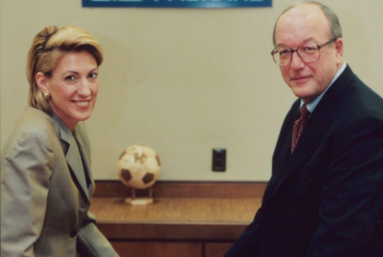 Carly Fiorina and Lew Platt seated on a table next to an HP laptop.